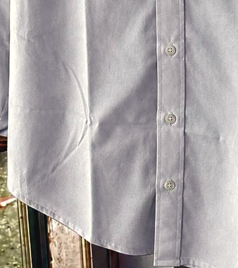 Close-up of a white woven cotton shirt showing the button placket, stitching and shirt-tail hem